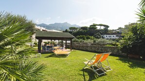 A grassy outdoor area with a gazebo, lounge chairs, and a view of mountains. - Hotel Park Victoria (Forio)