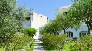 A pathway leading to a building with white walls and arched windows, surrounded by greenery and trees. - Hotel Park Victoria (Forio)