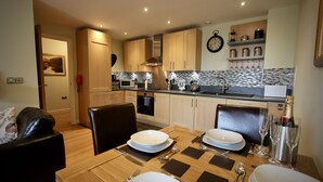 Une cuisine moderne dotée de meubles en bois, d’un four à micro-ondes et d’un coin repas aménagé pour quatre personnes, avec une table, des chaises et de la vaisselle.