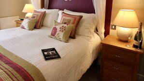 Un lit bien fait, avec du linge de lit blanc, un coussin décoratif, une table de chevet avec une lampe et un tableau encadré accroché au mur.