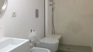 Un baño con lavamanos, dos inodoros, ducha y espejo.