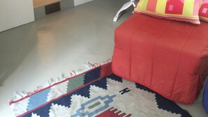 Una habitación con un sofá rojo, un tapete estampado, una silla blanca y un baño visible a través de un arco.