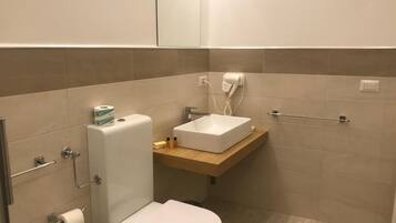 Een compacte, moderne badkamer met een toilet, een wastafel op een houten plank, een haardroger en een handdoekhouder.