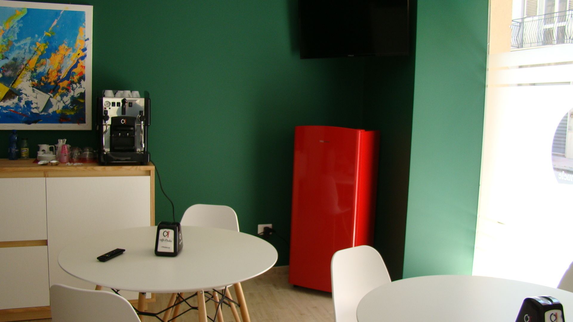 A room with a white table, chairs, a red refrigerator, a coffee machine, and a painting on the wall.