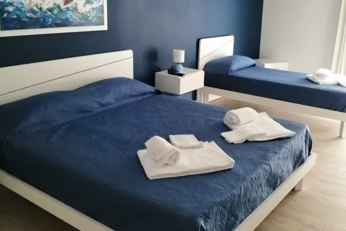 Quarto de hotel com uma cama grande, uma cama menor, um quadro na parede e uma luminária no teto.