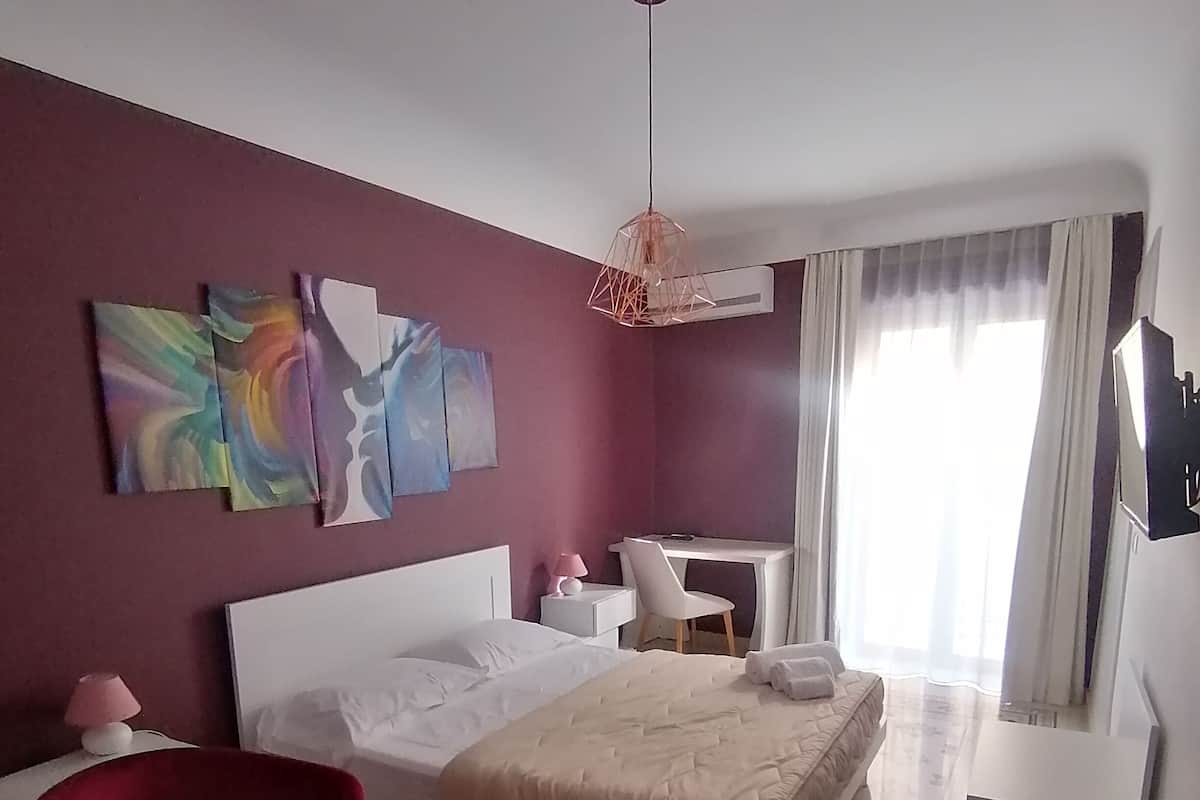 Quarto de hotel com cama, escrivaninha, cadeira e obras de arte na parede.