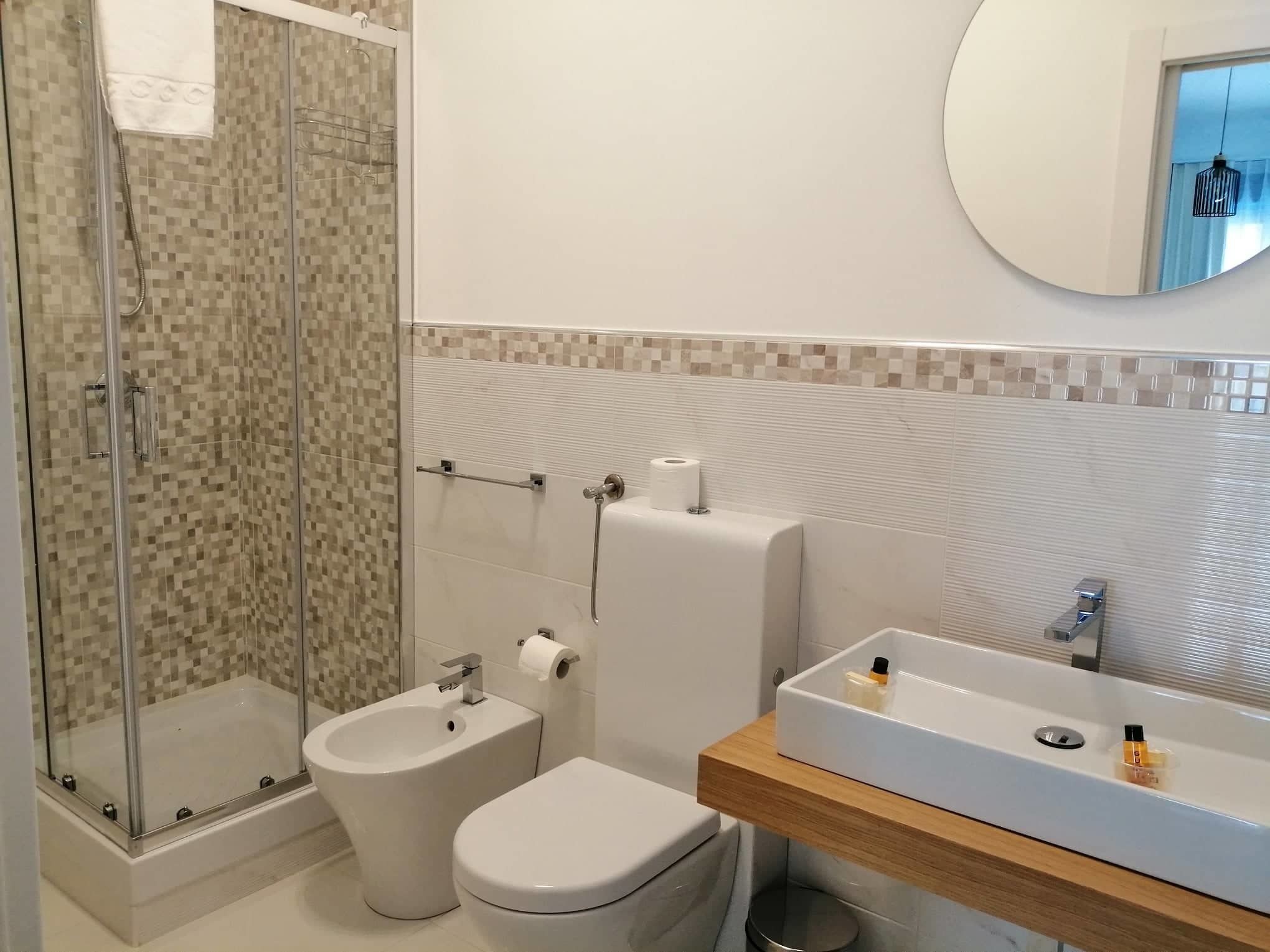 A modern bathroom with a glass shower enclosure, a bidet, a toilet, and a sink with a wooden countertop.