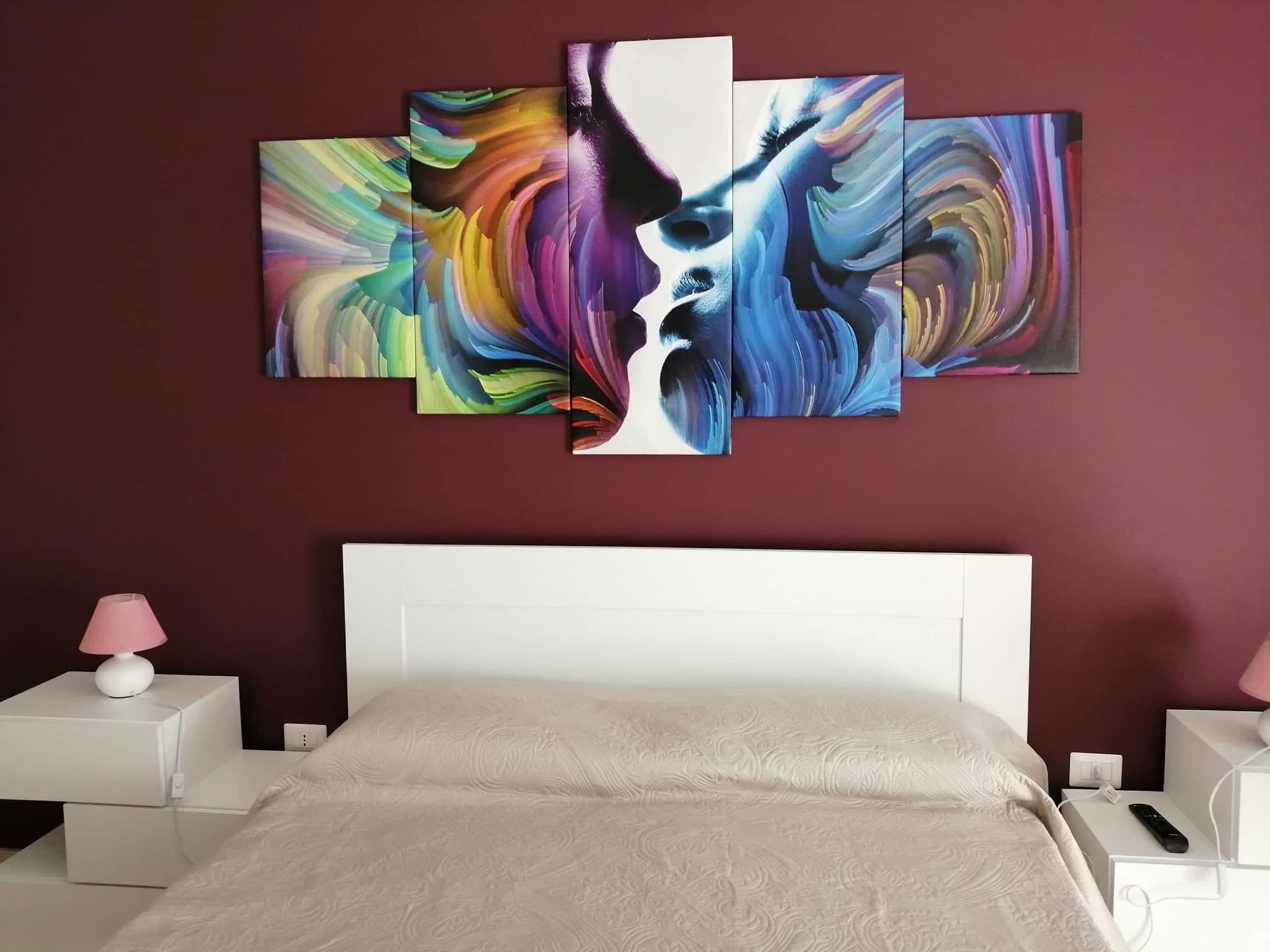 Une chambre d’hôtel avec un grand tableau abstrait au mur, un lit blanc et une table de chevet avec une lampe.