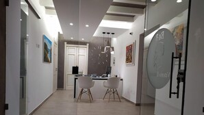 Een modern interieur met een receptiebalie, twee stoelen, een klok en een deur.