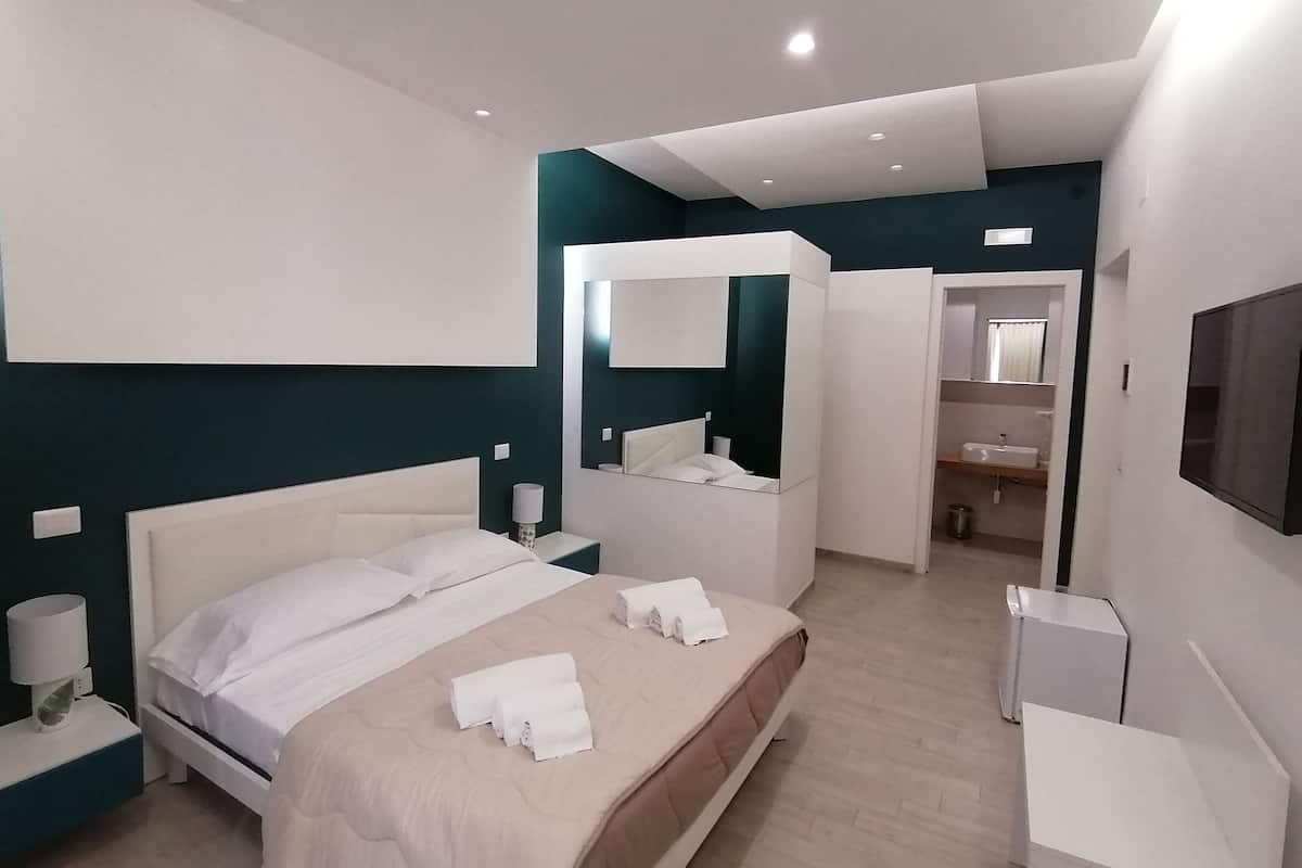 Quarto de hotel moderno com uma cama grande, mesa de cabeceira, espelho e televisão.