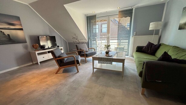 Un salon moderne doté d’un plafond en verre, d’un canapé vert, de deux fauteuils, d’une table basse et d’un téléviseur posé sur un meuble blanc.