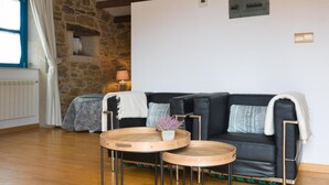 A cozy living room with a stone wall, a black leather sofa, two wooden side tables, and a lamp. - Casa de Amancio (Santiago de Compostela)
