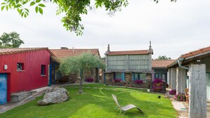 A courtyard with stone buildings, a lawn, and a chair. - Casa de Amancio (Santiago de Compostela)