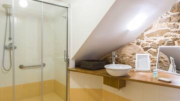 A bathroom with a glass shower enclosure, a sink with a stone wall backdrop, and a wooden countertop.