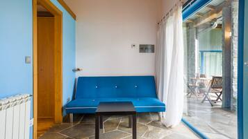 Une pièce avec un canapé bleu, une petite table et une porte vitrée donnant sur un espace extérieur équipé d’une table et de chaises.