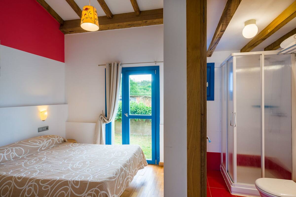 A bedroom with a bed, a bathroom with a shower, and a door leading outside.