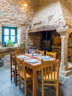A stone-walled dining area with a wooden table set for four, surrounded by chairs. - Casa de Amancio (Santiago de Compostela)