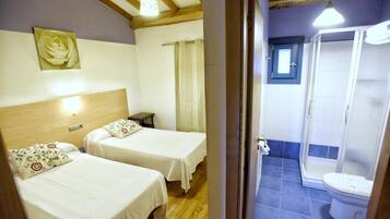 Ein Zimmer mit zwei Betten, einem Holz-Kopfteil, einer Wandleuchte sowie einem Badezimmer mit Dusche und Toilette.