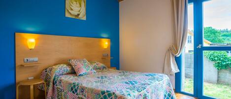 A bedroom with a wooden headboard, a colorful quilted bedspread, a small bedside table, and a window with curtains.