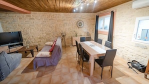 Um quarto acolhedor com parede de pedra, teto de madeira, televisão, sofá, mesa de jantar com cadeiras e janela com cortinas.