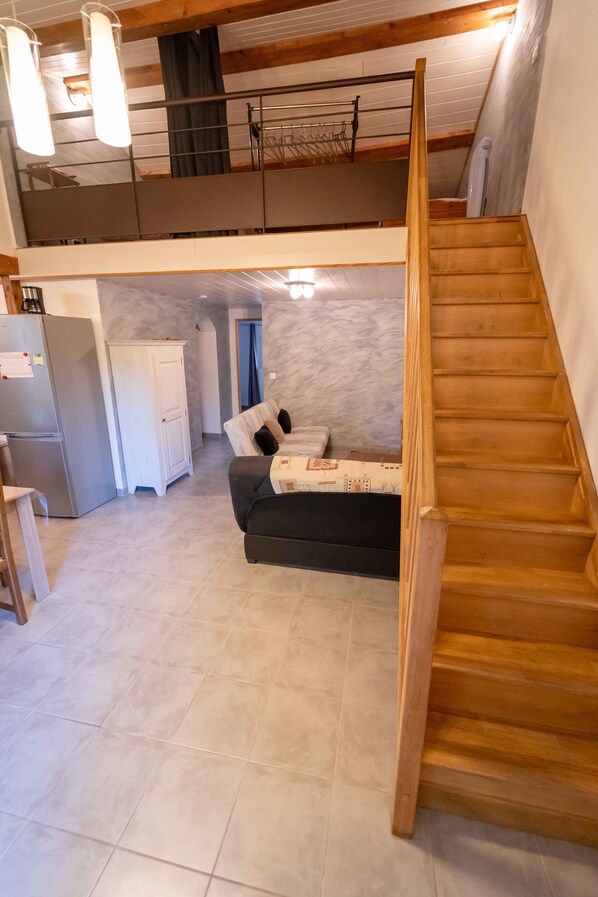 A spacious living area with a wooden staircase, a sofa, and a kitchen area with a refrigerator and cabinets. - ----- High Gite ------ (Codognan)