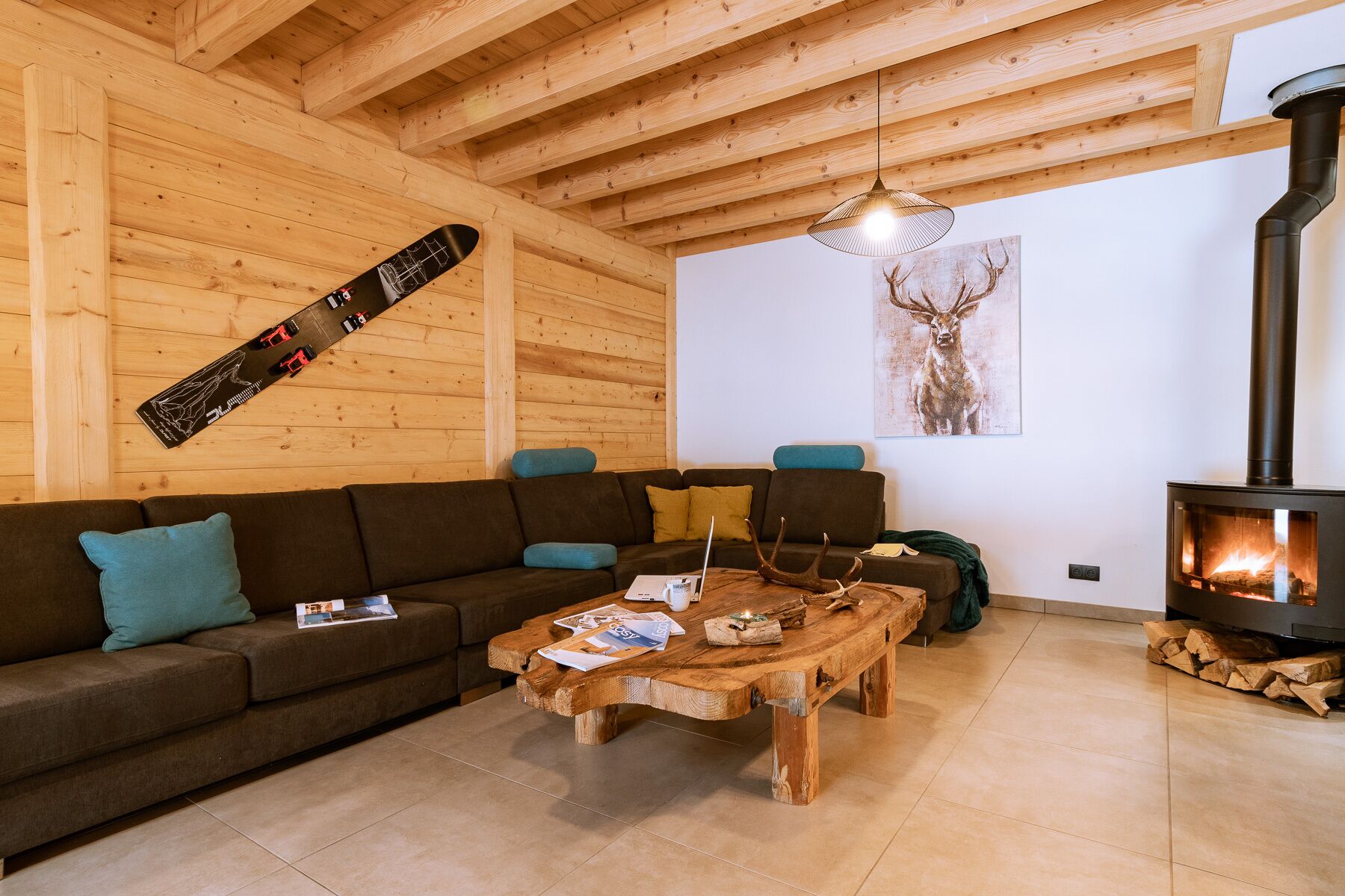 A cozy living room with a wooden ceiling, a sofa, a coffee table, a fireplace, and a deer painting on the wall.