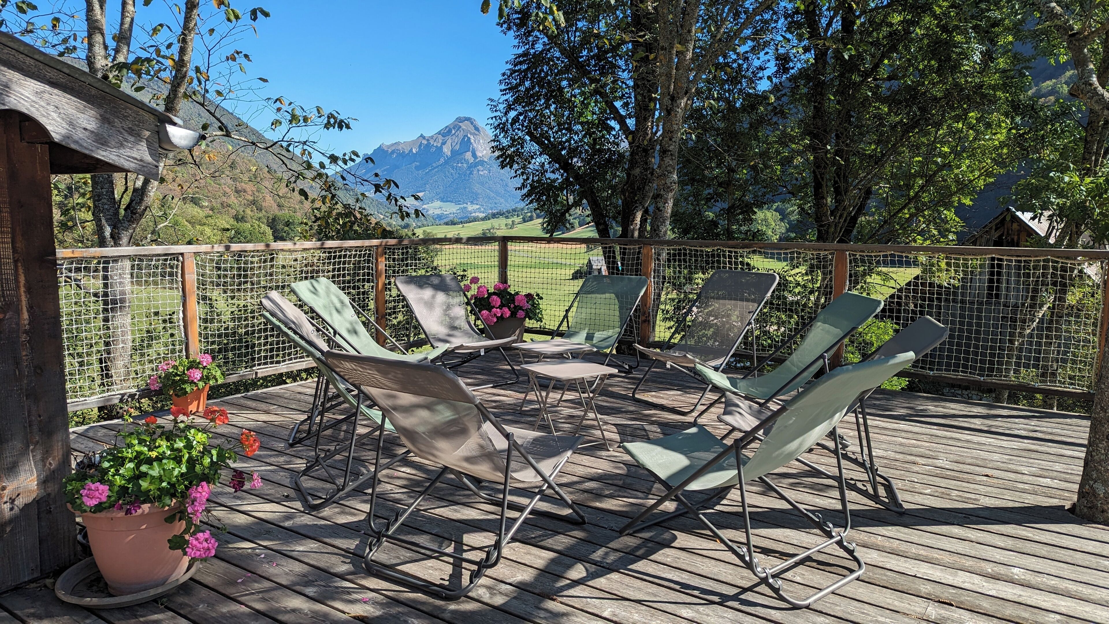 Una terraza de madera con mobiliario exterior, vista a las montañas y una valla de madera.