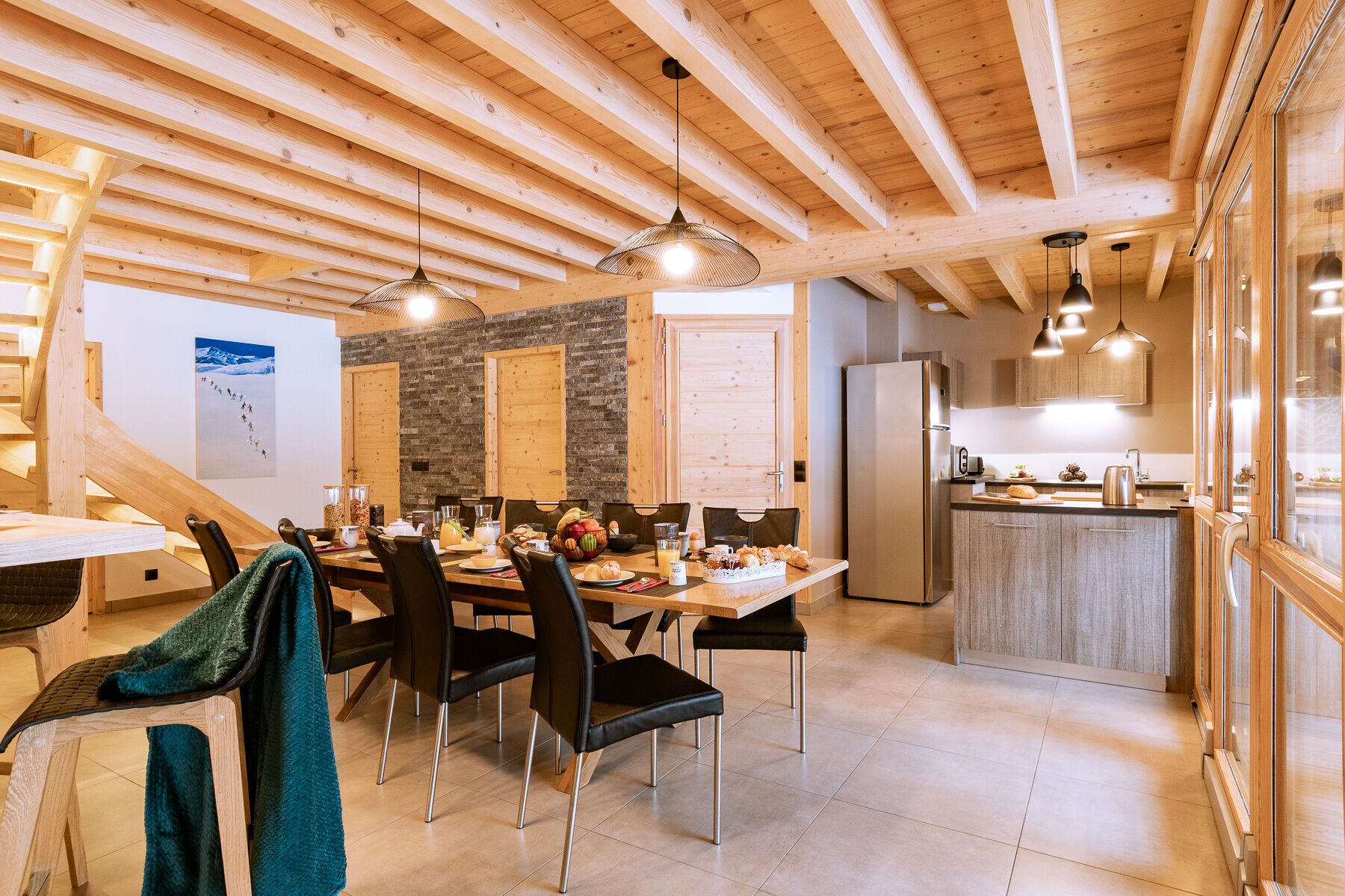 Een ruime eethoek met een houten tafel en stoelen, een keuken met moderne apparatuur en een trap naar een ander niveau.