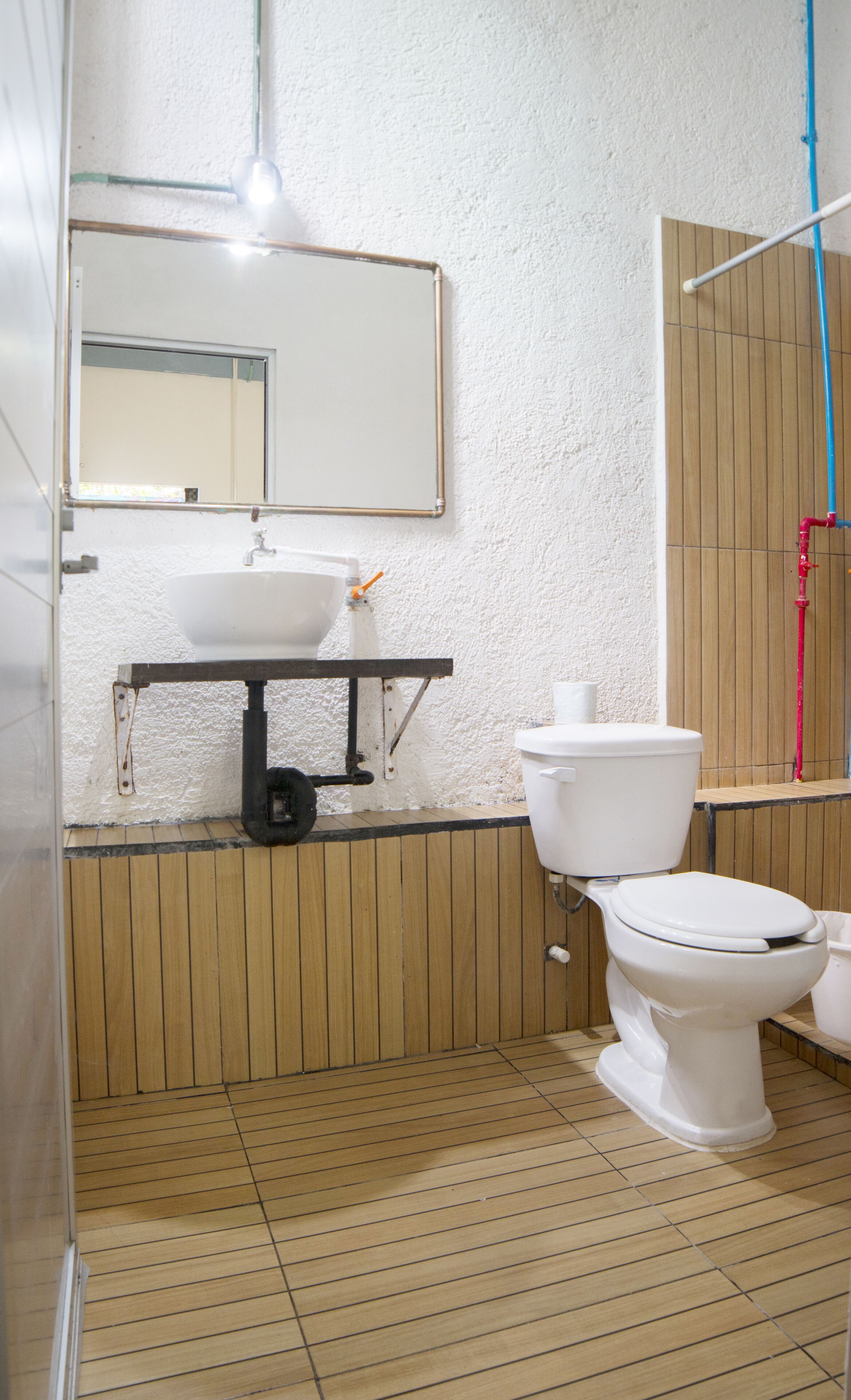 A bathroom with a wooden floor, a white sink, a toilet, and a mirror above the sink.