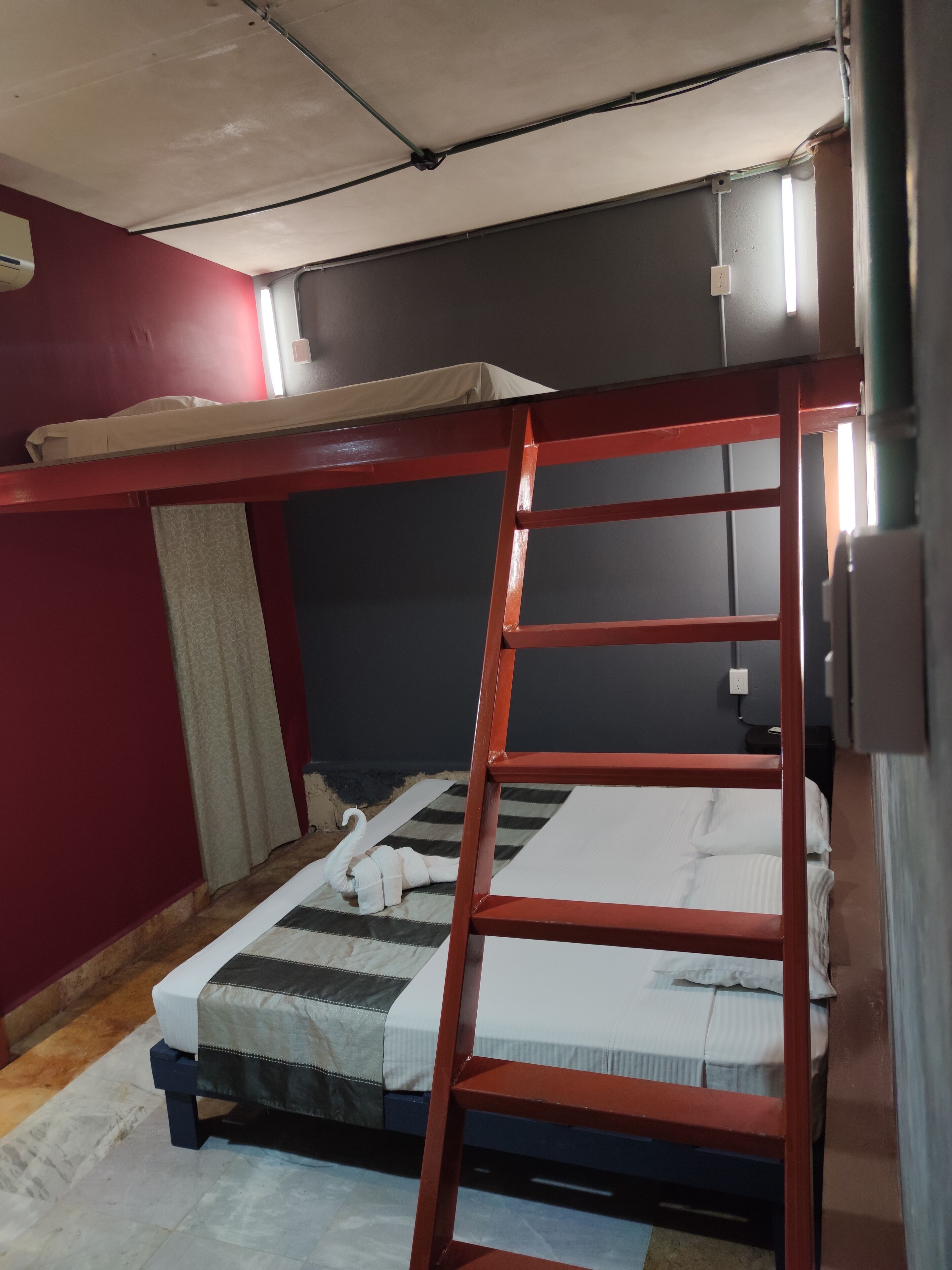 Un letto a castello con una scala, una finestra con tende e una parete rossa.