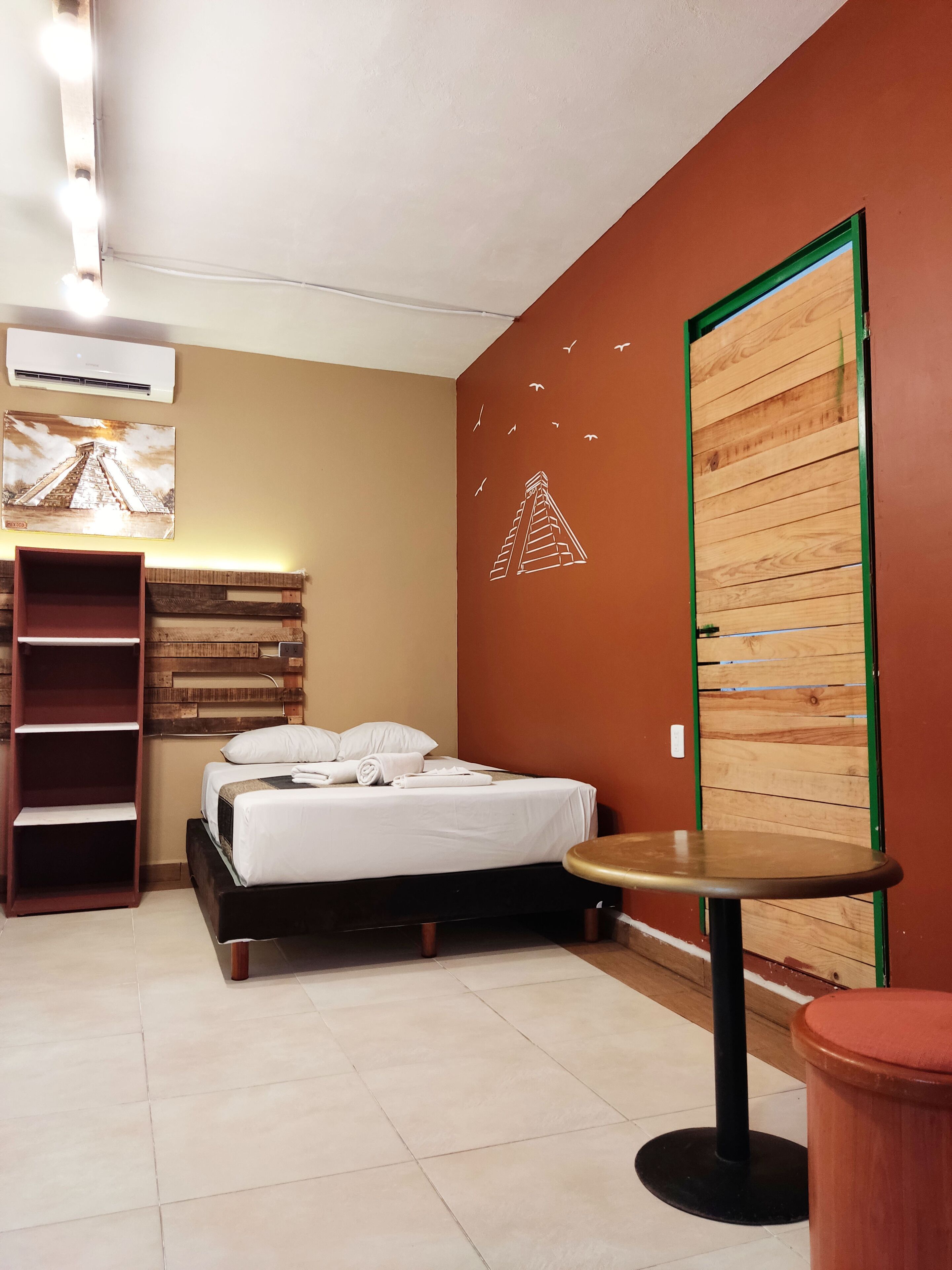 Una habitación de hotel con una cama, un armario de madera, una mesita redonda y un estante.