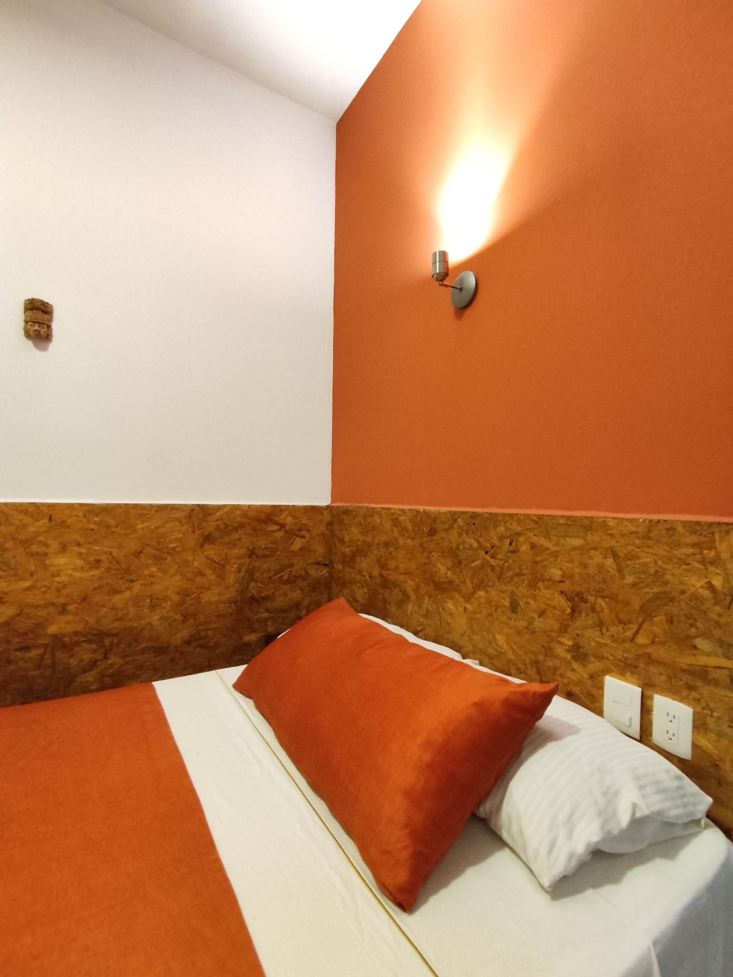 Et hotelværelse med en seng, en orange væg og en vægmonteret lampe.