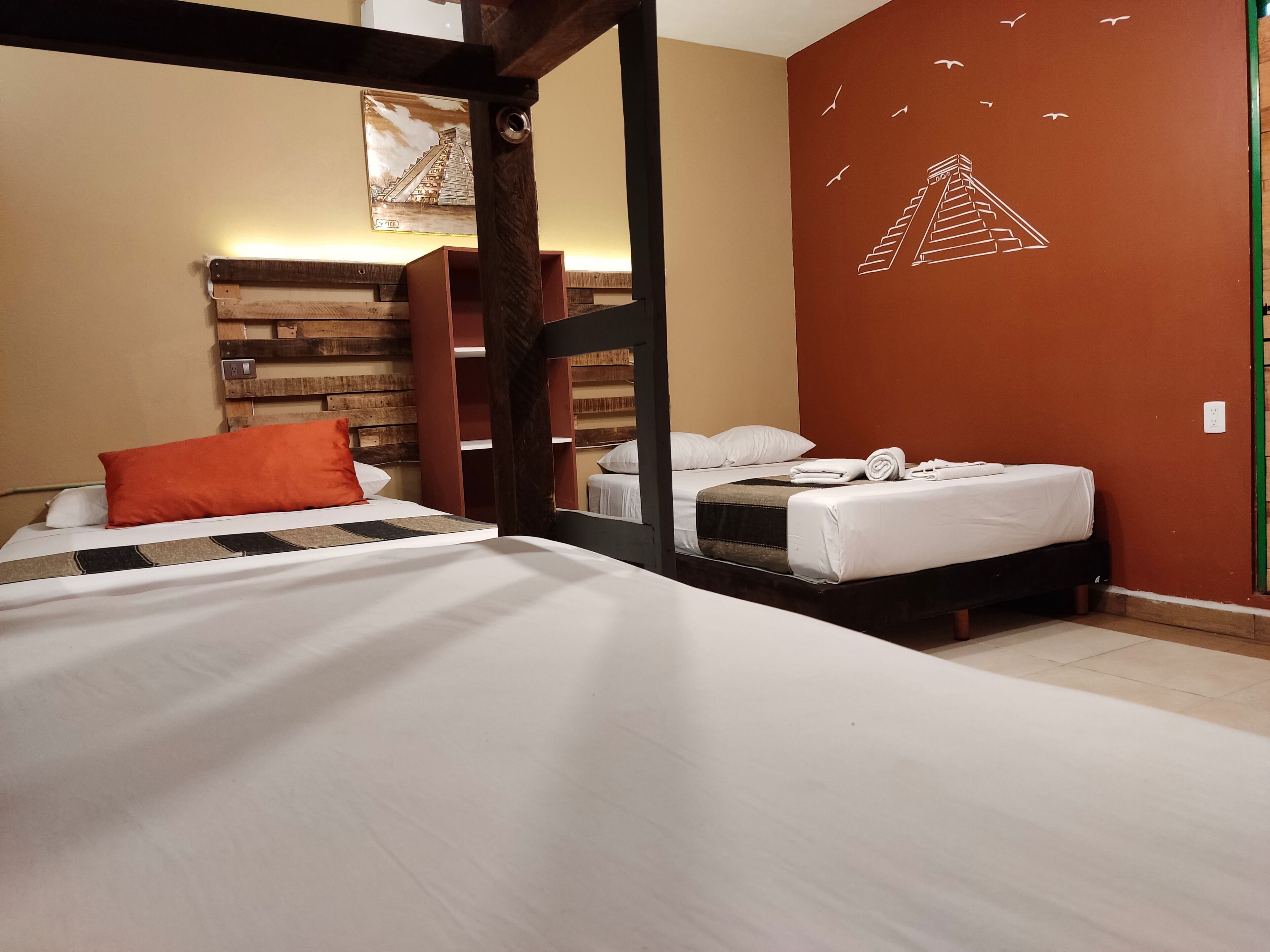A hotel room with two beds, wooden headboard, a mural of a pyramid, and a green wall.