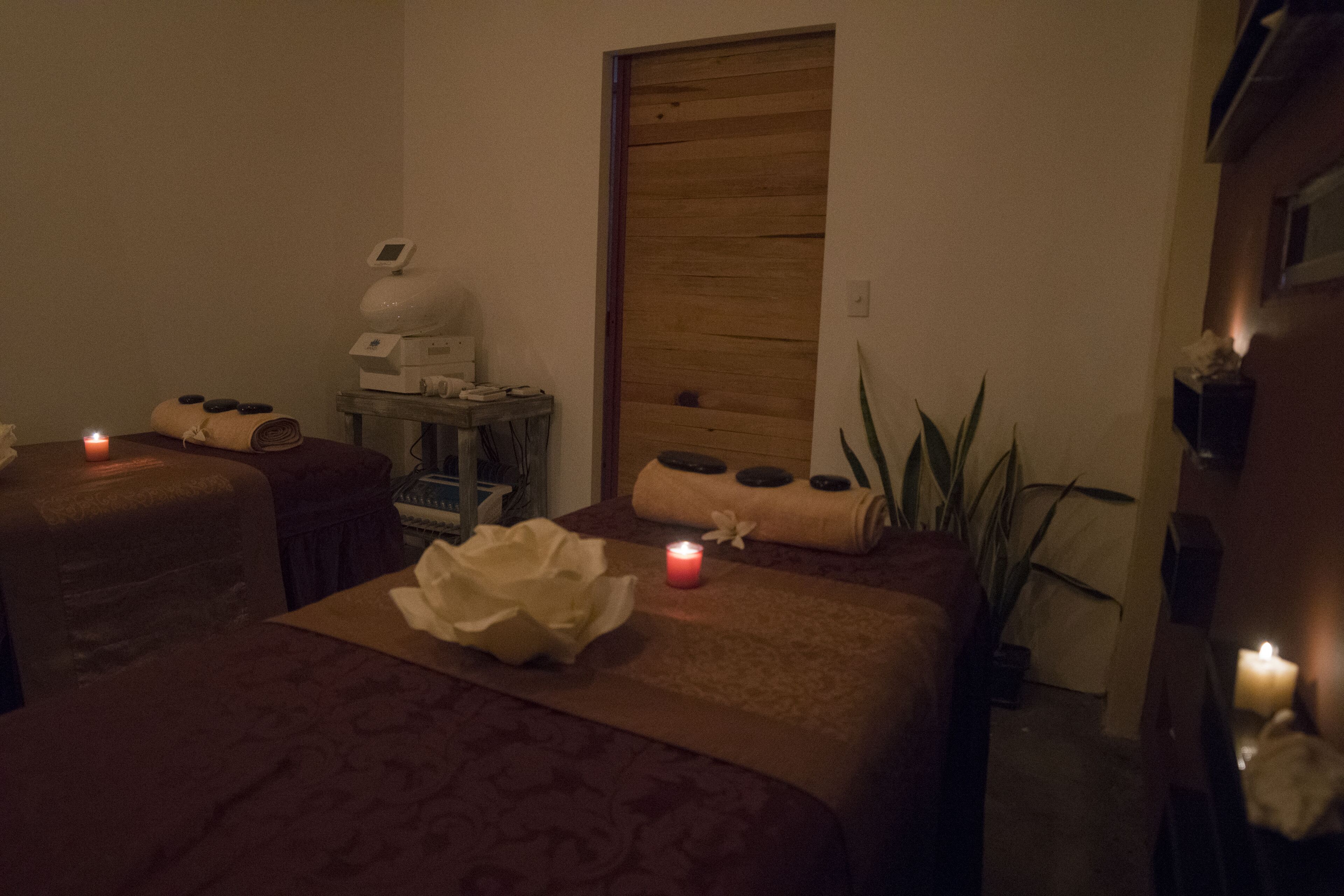 Een wellnessruimte met twee bedden, een massagetafel, een houten deur en een klein tafeltje met een massageapparaat.