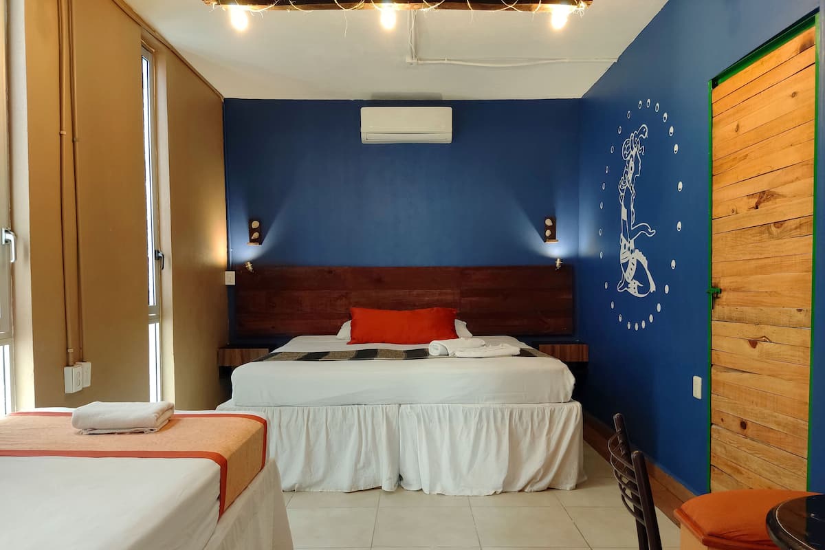 Una habitación de hotel con cama, una silla, una mesa y una pared con un mural.