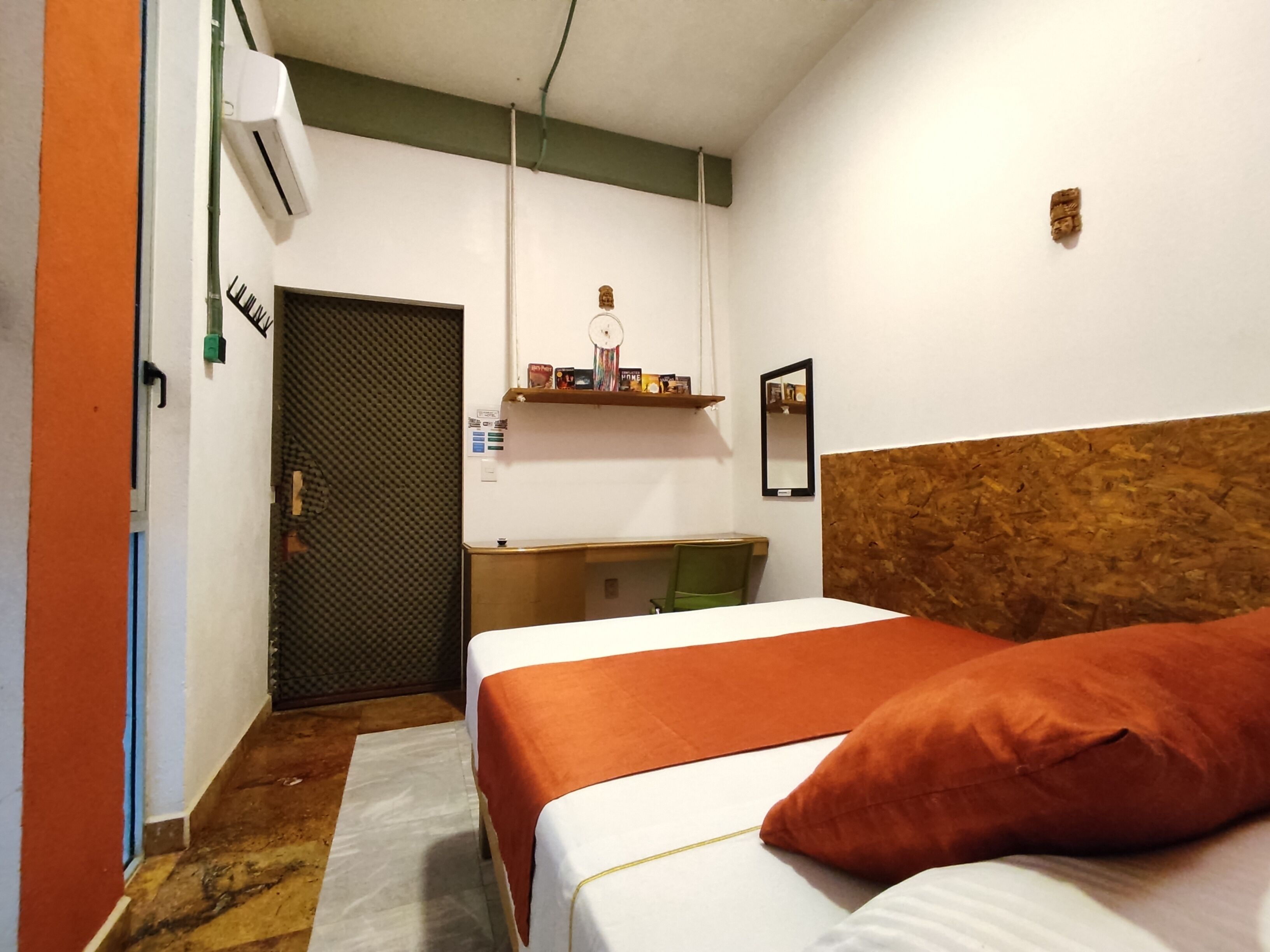 A hotel room with a bed, a desk, and a chair. There is a door and an air conditioning unit on the wall.