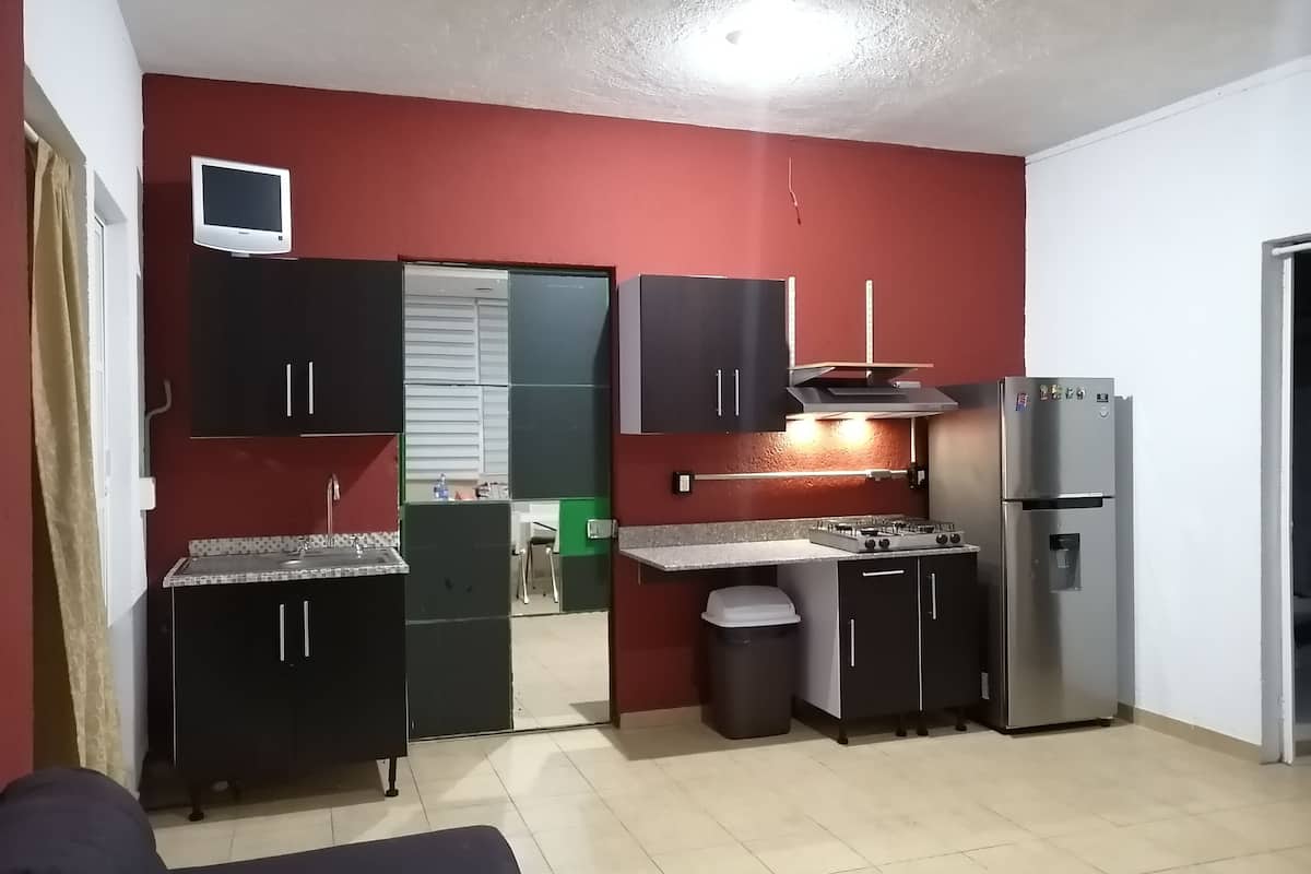 Cocina compacta con paredes rojas, estufa integrada, refrigerador y un lavamanos pequeño.