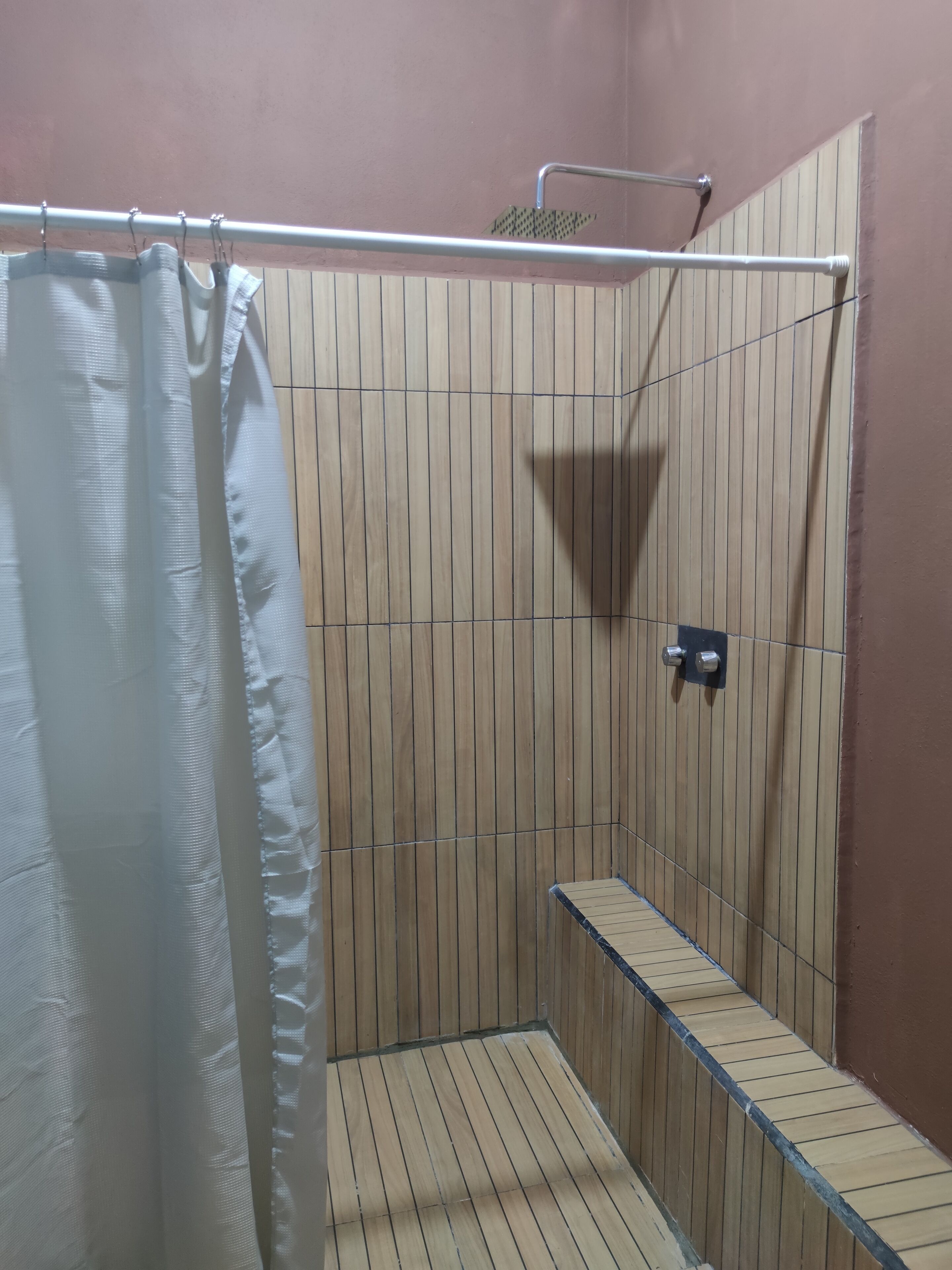 Zona de ducha con pared de paneles de madera, cabezal de ducha metálico y cortina de ducha blanca.