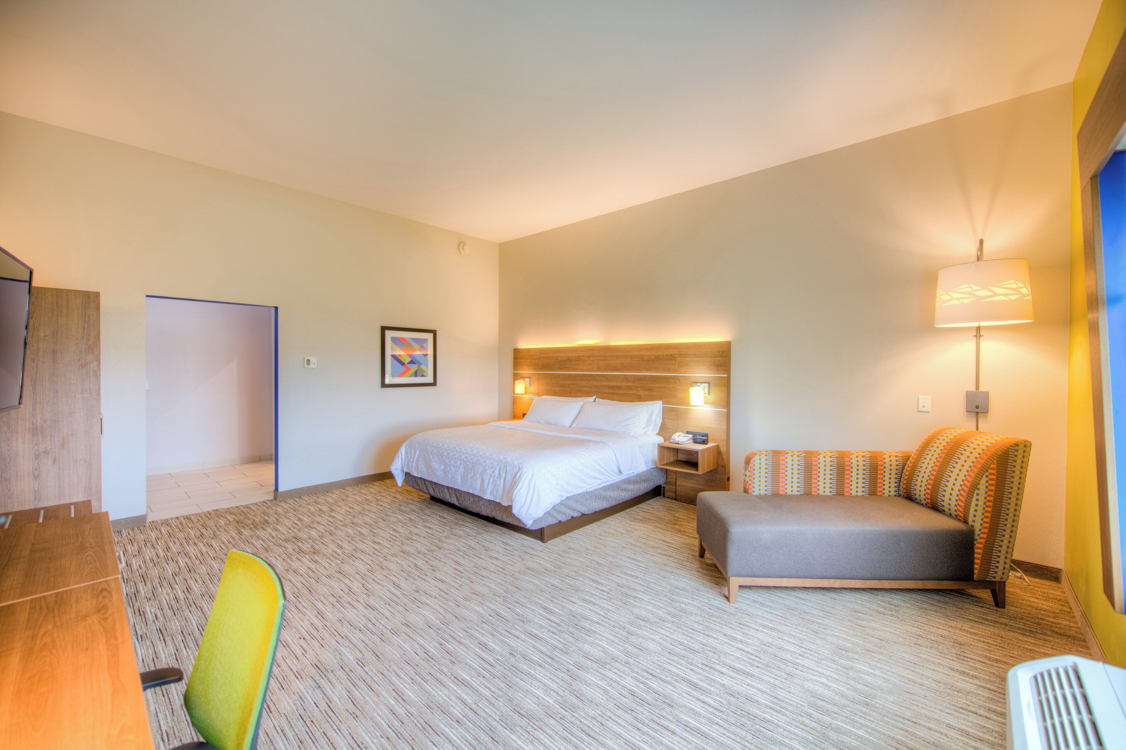A hotel room with a bed, bedside table, lamp, and a sofa.
