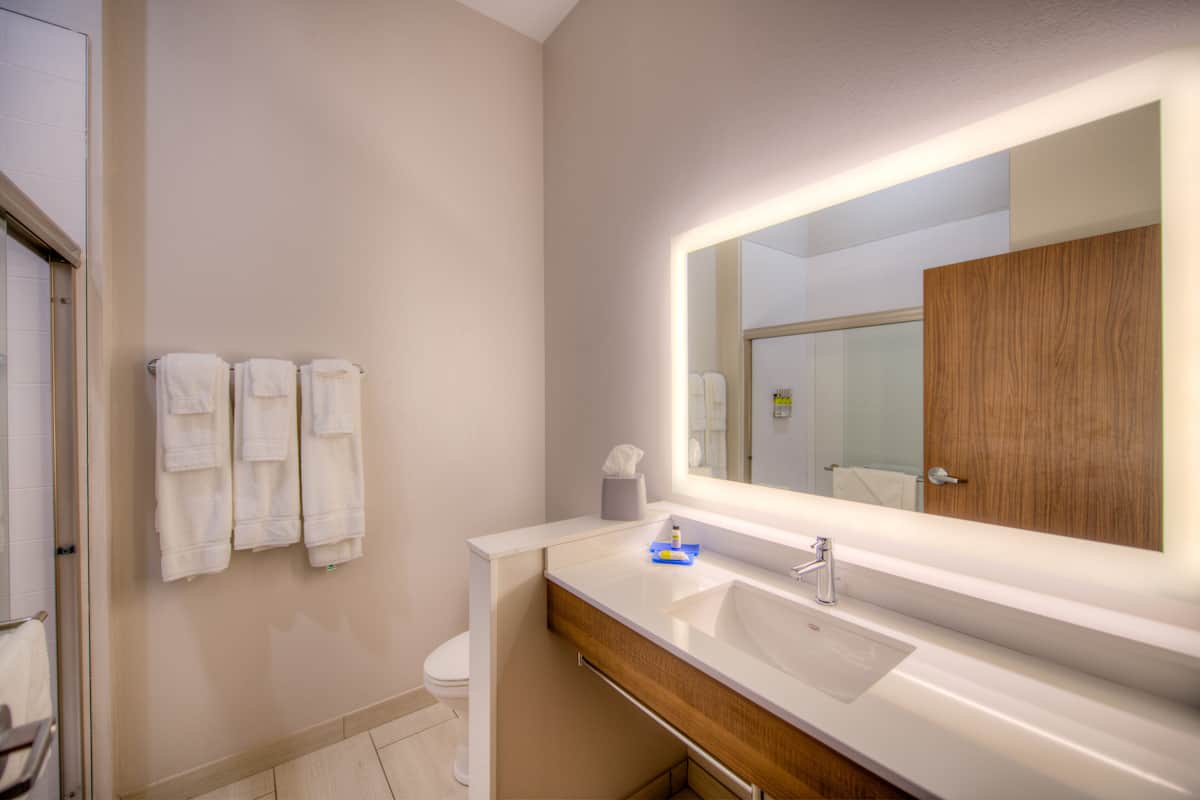 A modern bathroom with a white sink, a large mirror, and two white towels hanging on the wall.