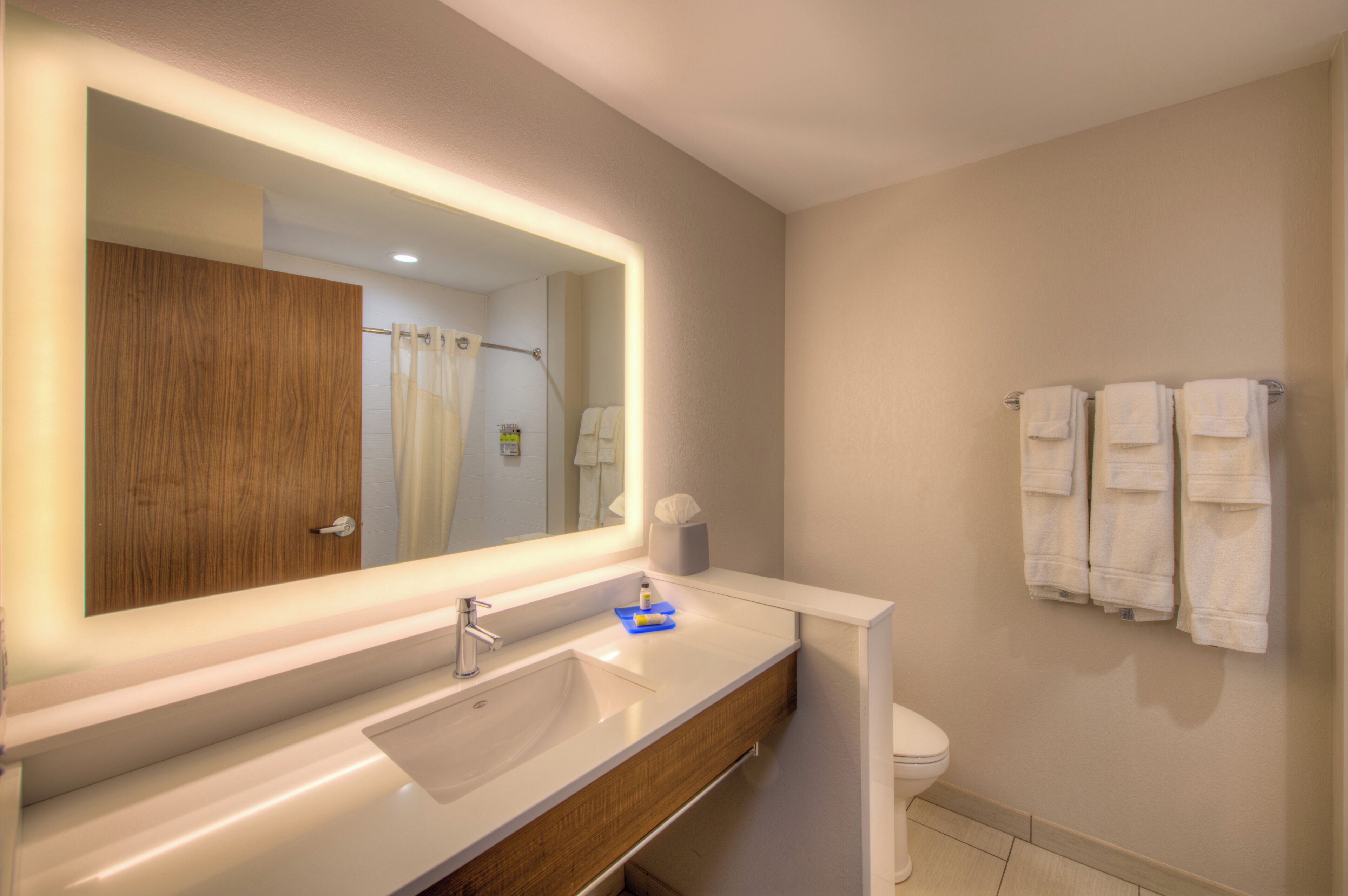 Un baño moderno con un espejo grande, un lavamanos, un inodoro y un perchero para toallas.