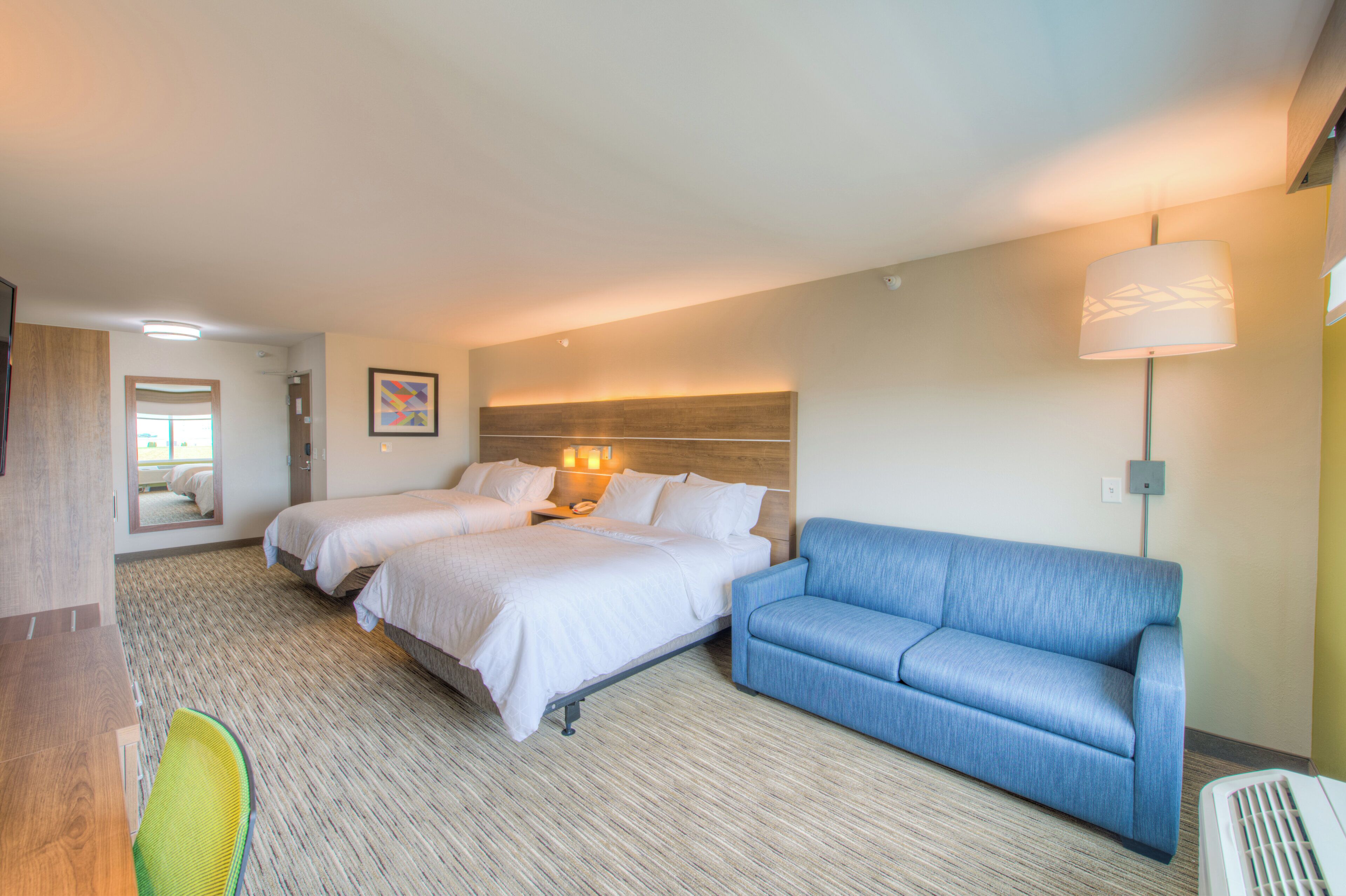 Ett hotellrum med två sängar, en blå soffa, ett skrivbord med en stol och ett stort fönster.