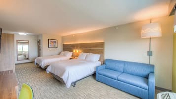 A hotel room with two beds, a blue sofa, a desk with a chair, and a large window.