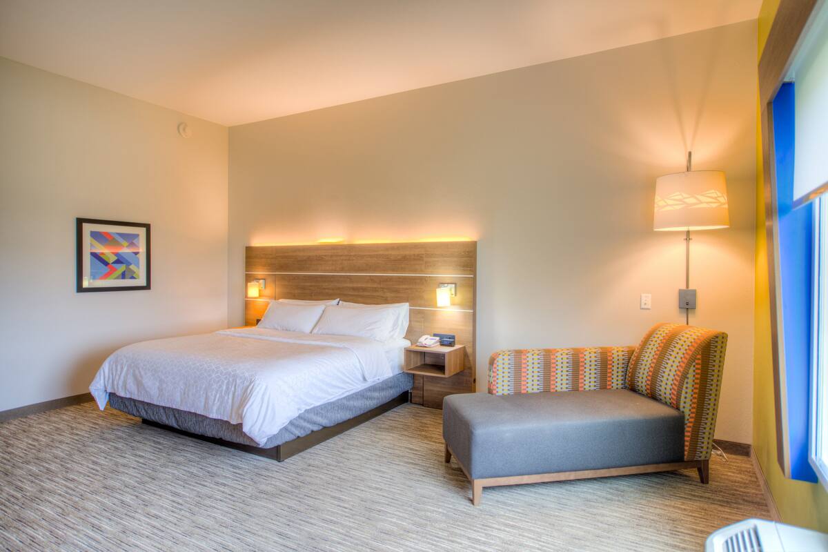 A hotel room with a large bed, a sofa, a wall-mounted lamp, and a framed picture on the wall.