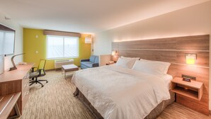 Quarto de hotel com uma cama grande, uma escrivaninha com cadeira, uma mesinha e uma janela com persianas.