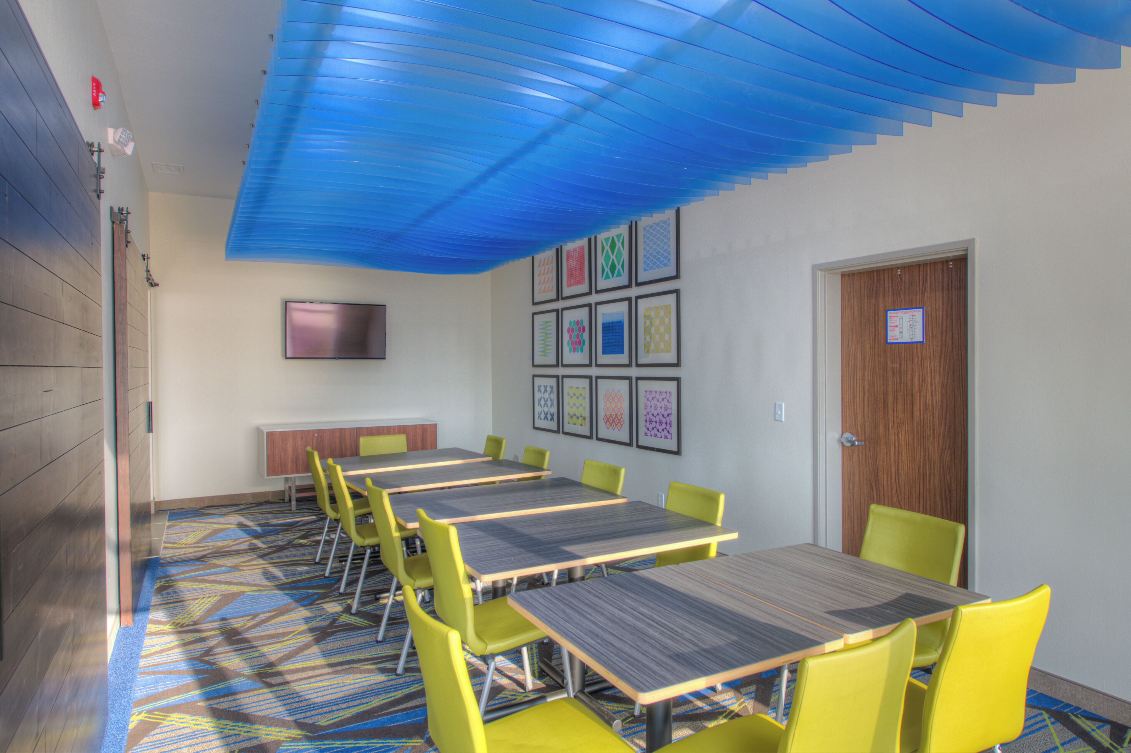 A conference room with tables and chairs, a flat-screen TV, and framed artwork on the wall.