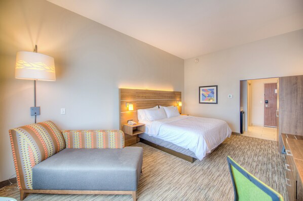 A hotel room with a bed, a desk, a chair, a lamp, and a picture on the wall.