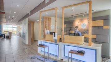 A reception area with a wooden reception desk, a digital screen, and a seating area with chairs.