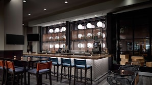 Un espace bar moderne doté d’un comptoir central, de tabourets de bar et d’un coin salon avec des tables et des chaises.