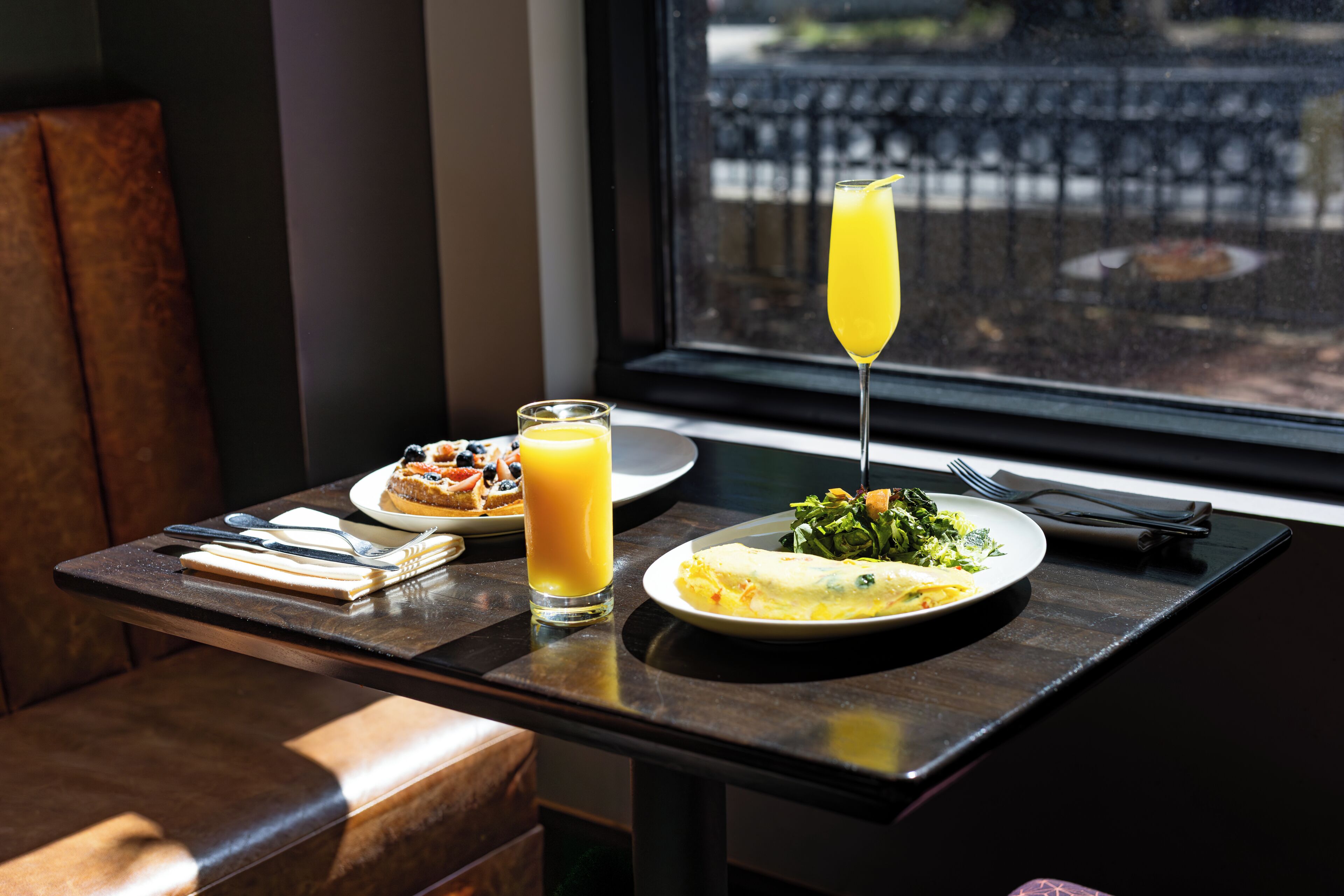 A table with breakfast items, a glass of orange juice, and a glass of orange juice with a straw.